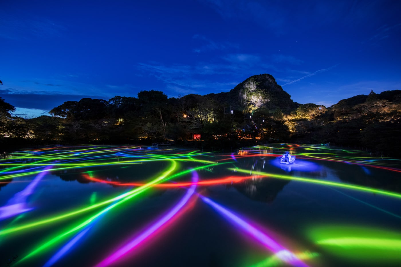 Outside installation: Set on a large pond/lake with the backdrops of mountains is the light projection of fish - in particular the bright rainbow coloured paths they, and the boats, have made.